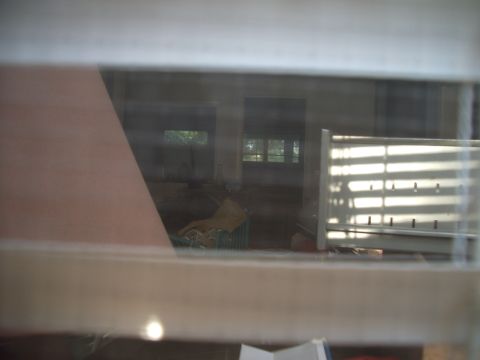 1978 Ford Bronco - A view through blinds reveals the interior of a building with a large object and the Supermotors.net logo.