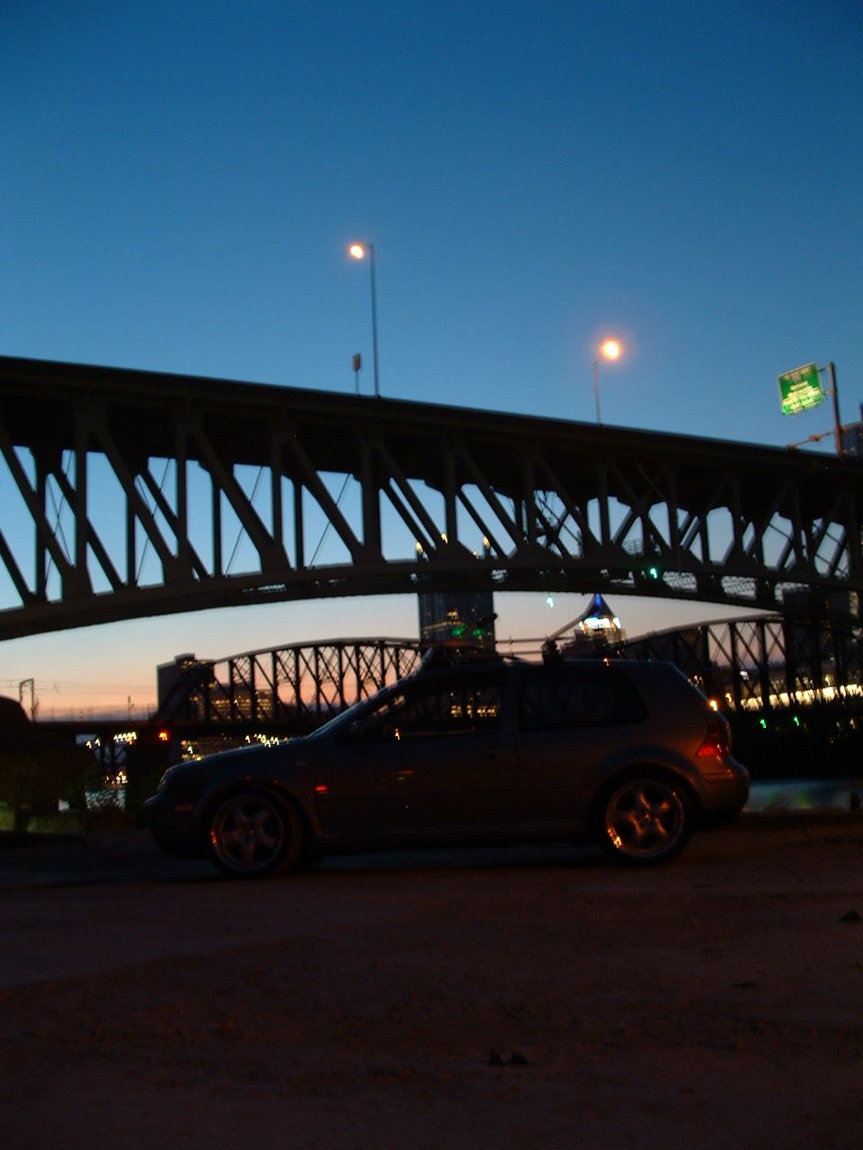 Dark hatchback parked by a bridge at dusk
