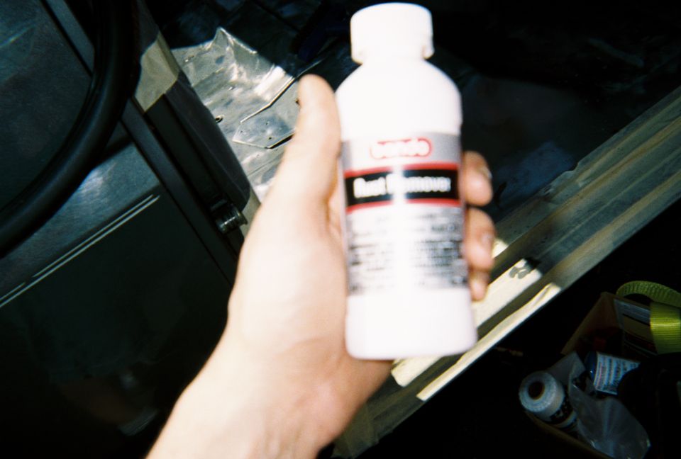 Hand holding a small white plastic bottle of fluid over a dark vehicle interior under work