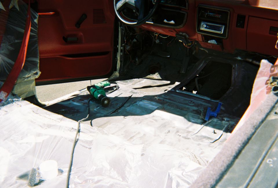 Stripped truck cab interior with bare floor pan, red door panels, drill on plastic sheeting