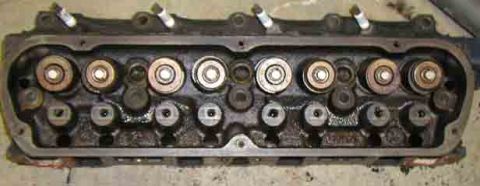 1988 Ford Bronco - Used cast-iron V8 cylinder head sitting rocker-side up on a concrete floor, showing eight valve spring assemblies with rusty retainers and…
