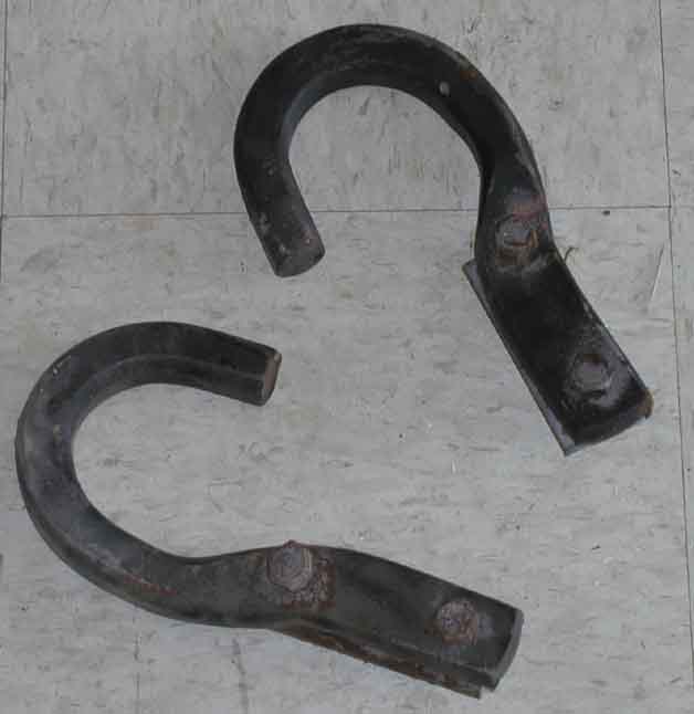 Pair of black forged steel tow hooks with two-bolt mounting flanges on a plywood floor