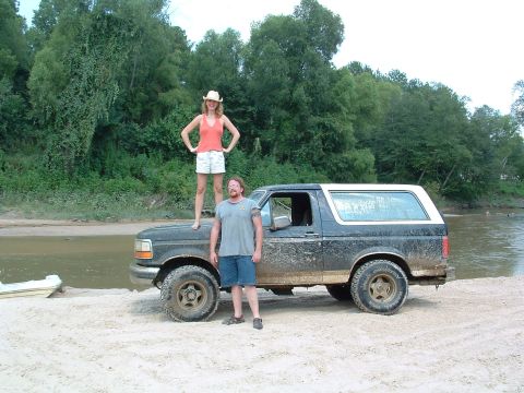 1993 Ford Bronco - A 1993 Ford Bronco sits on a sandy shore next to a river, with two people posing with the vehicle.