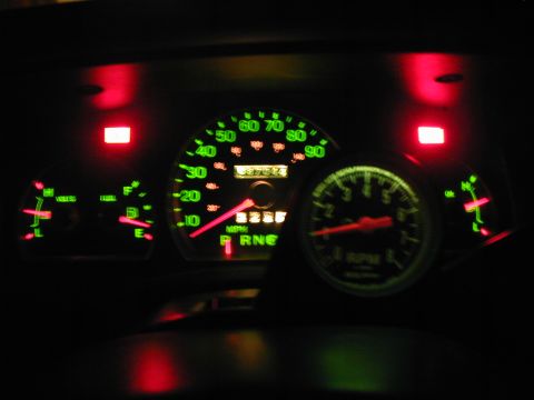 2000 Ford Crown Victoria - Night shot of a lit instrument cluster with green-glowing gauge faces and red needles, a 90 MPH speedometer with mechanical odometer and PR…
