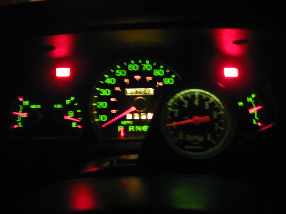 Green-lit instrument cluster at night with speedometer, tachometer and red needles
