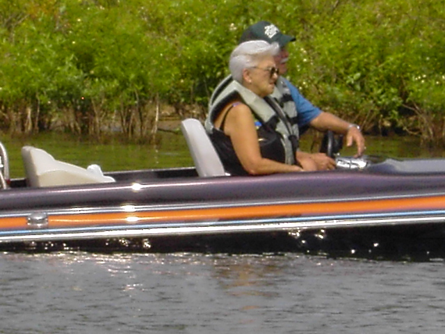Two people in a boat on the water, with green foliage in the background