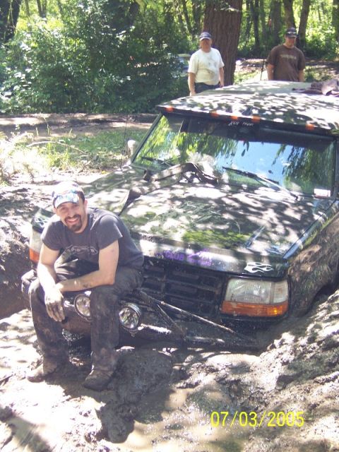 1995 Ford Bronco - A man poses on the hood of a mud-covered Ford Bronco that is stuck in a muddy off-road trail.