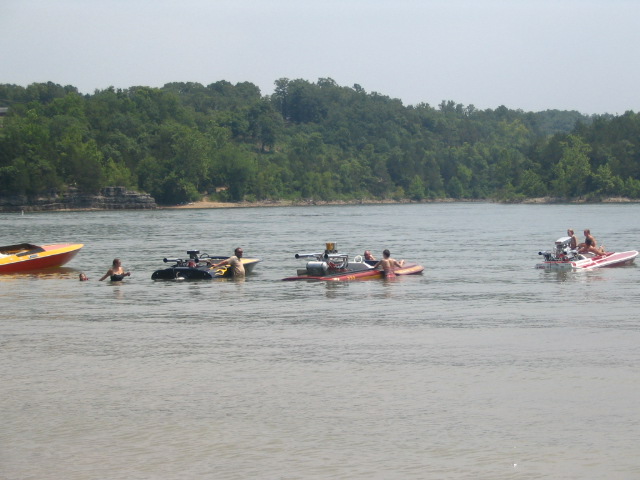 Row of open flat-deck speedboats with exposed engines floating in shallow lake water