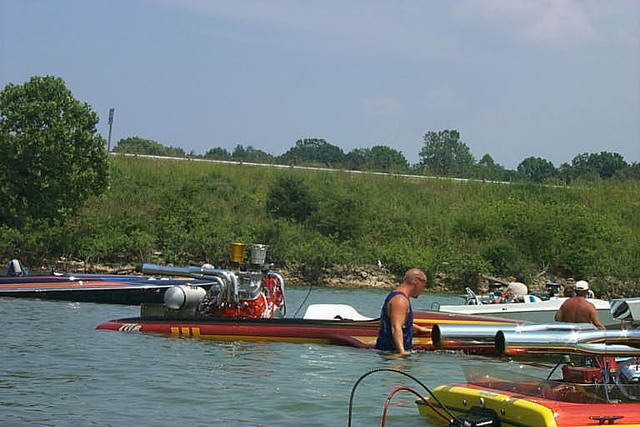 Red flat-deck race boat with exposed supercharged engine in shallow lake water