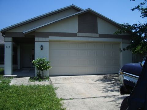 1978 Ford Bronco - A residential house with a large garage door is shown, with a portion of a blue vehicle visible in the foreground.