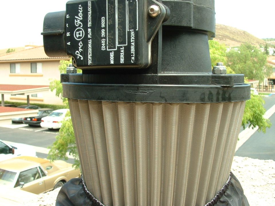 Close-up of a Pro-Flow air filter with text labels. Cars are parked in the background