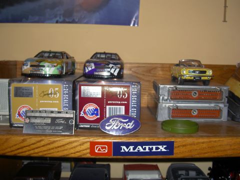 1988 Ford Bronco - A collection of model cars and electronic components are displayed on a wooden shelf, with various racing-themed boxes and stickers visible.