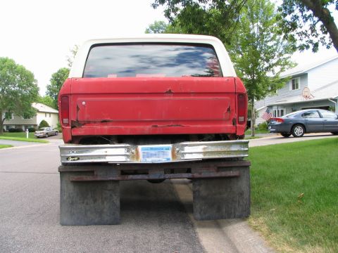 1978 Ford Bronco - The rear of a red SUV is shown with a custom bumper and mud flaps, parked on a residential street.