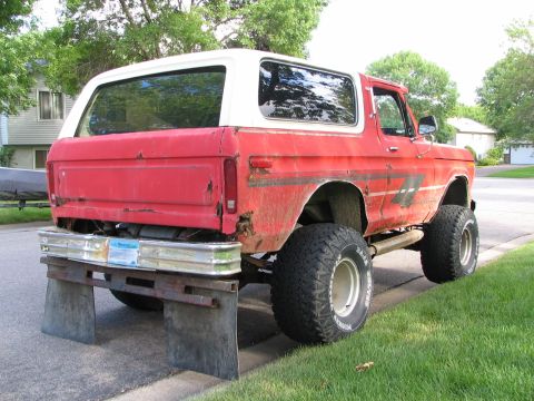 1978 Ford Bronco - This red 1978 Ford Bronco with a white top is lifted with large tires and mud flaps.