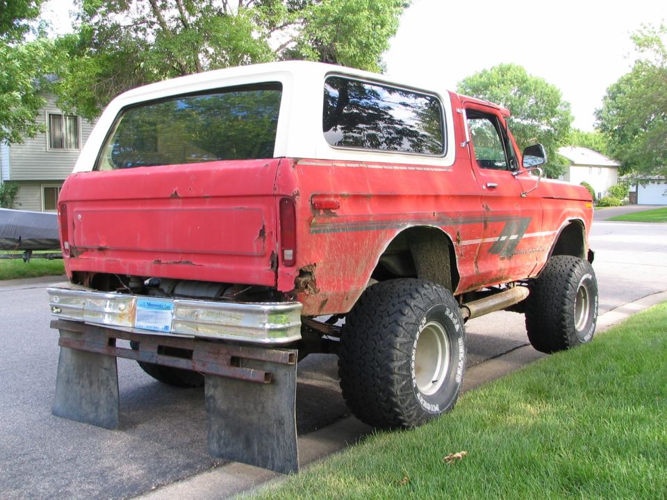 Red 1978 Ford Bronco with a white top, lifted with large tires, seen from the rear