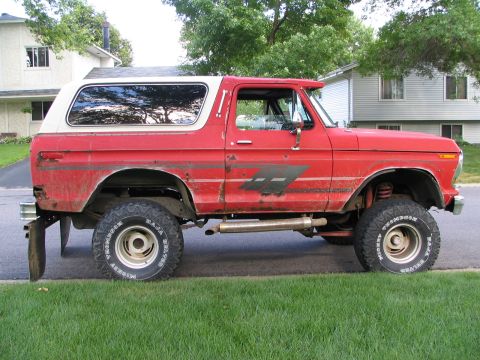 1978 Ford Bronco - This red 1978 Ford Bronco features a white removable top and off-road tires, seen parked on a grassy lawn.