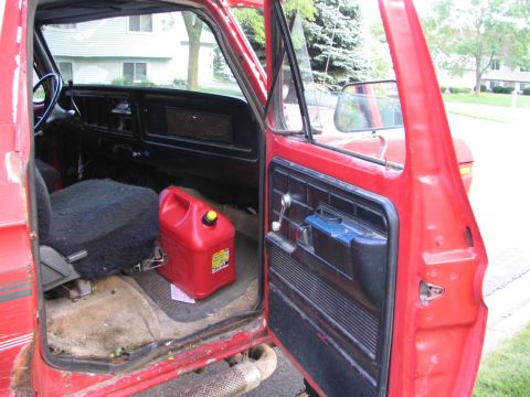 1978 Ford Bronco - The interior of a red pickup truck shows a gas can and a door-mounted storage bin.