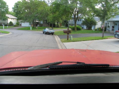 1978 Ford Bronco - A blue coupe is parked on the side of a residential street. The photo is taken from the perspective of another vehicle.