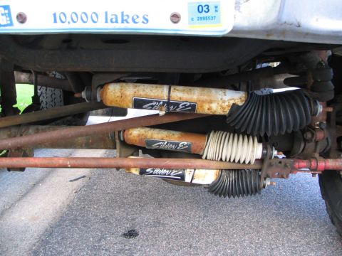 1978 Ford Bronco - Close-up of the undercarriage, showing rusty shocks and steering components, with a Minnesota license plate in the background.