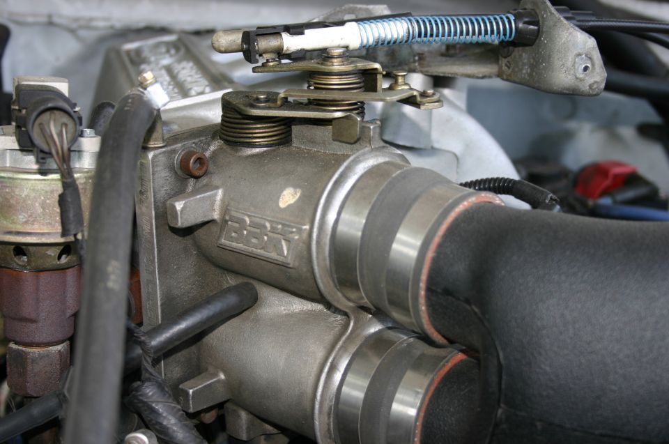 BBK twin-bore throttle body with black intake tube and throttle linkage in a 1994 Ford Bronco engine bay