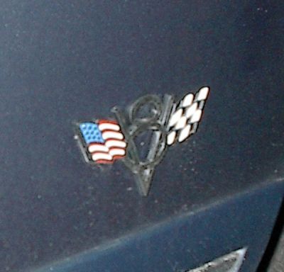 1985 Mercury Grand Marquis - A V8 emblem the American flag and a checkered flag is attached to a dark surface.