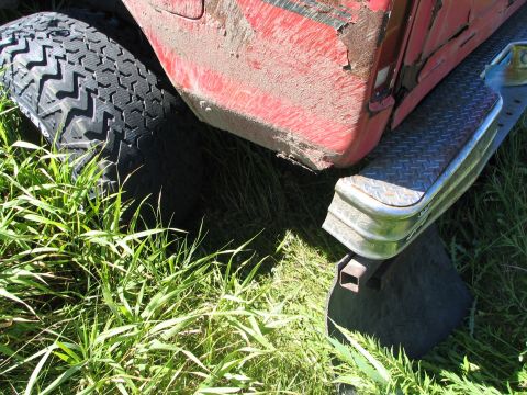 1978 Ford Bronco - Close-up view of a red vehicle's fender and tire, partially obscured by grass.