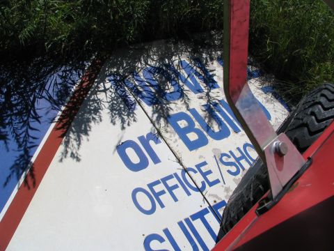 1978 Ford Bronco - A sign with text 'or BUILD OFFICE/SUITES' is partially visible, with shadows from trees overhead.