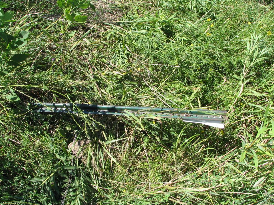 Green metal fence T-posts lying in tall grass