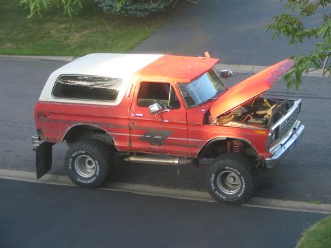 1978 Ford Bronco - This lifted 1978 Ford Bronco features a two-tone red and white paint scheme and off-road tires, with its hood open revealing the engine bay.