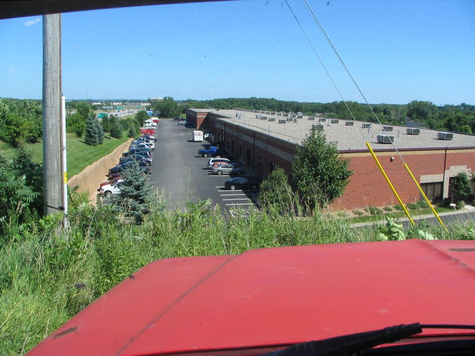 View of a parking lot and brick building from a red vehicle's hood, with many cars parked in rows
