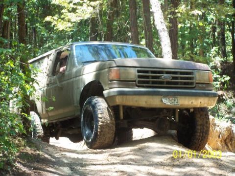 1987 Ford Bronco - A 1987 Ford Bronco navigates a wooded trail with large tires.