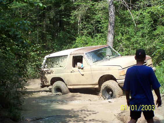 Tan 1987 Ford Bronco stuck in mud with a man watching