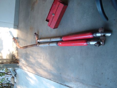 1994 Ford Bronco - Dual-exhaust system laid out on a garage floor before installation (photo rotated 90 degrees), with two red-painted glasspack-style muffler…