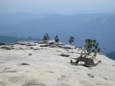 1967 Ford Bronco - A person contemplates the vast landscape from a rocky peak, with distant mountains fading into the haze.