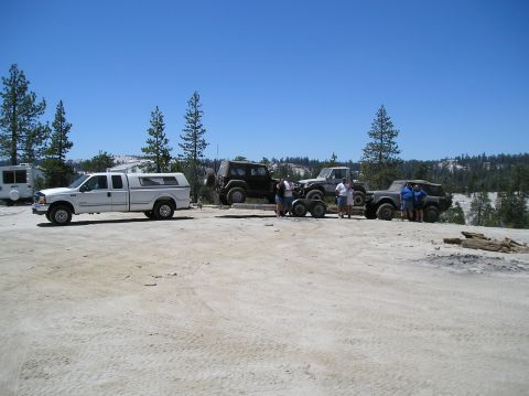 1967 Ford Bronco - A group of off-road vehicles and a pickup truck are gathered on a dusty lot under a clear blue sky.