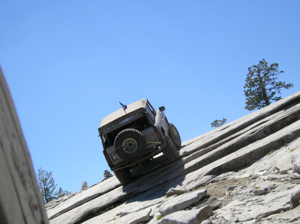1967 Ford Bronco climbing a steep, rocky incline under a clear blue sky