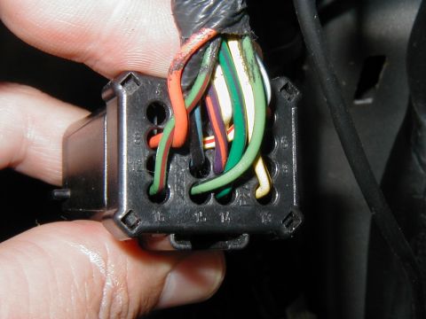 2002 Ford Excursion - A hand holds a wiring harness connector with multiple colored wires, some showing signs of wear.