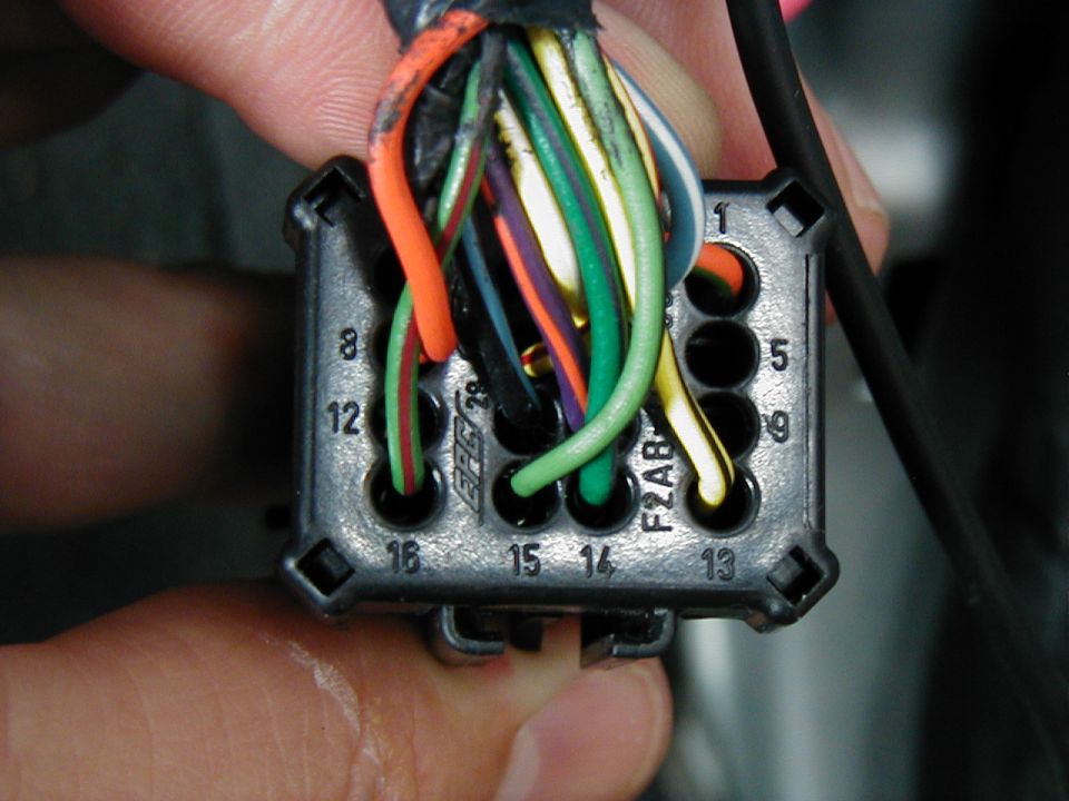 Hand holding black multi-pin wiring connector with numbered cavities and colored wires
