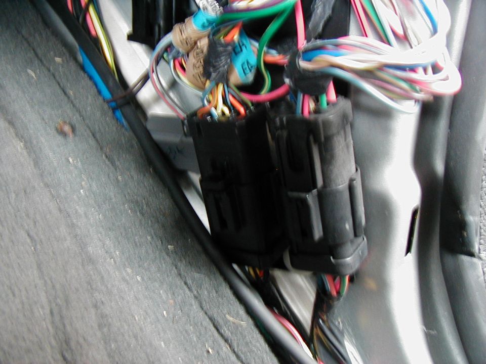 Two black multi-pin connectors amid a bundle of colored automotive wiring