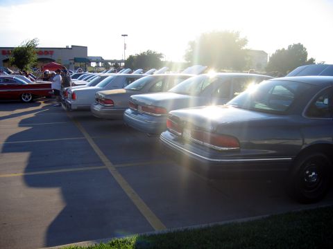 2000 Ford Crown Victoria - A line of Ford Crown Victorias are parked in a lot during a meet-up event.