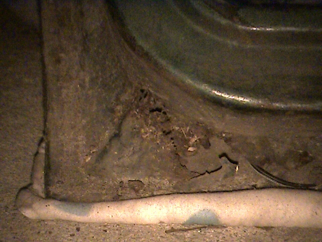 Close-up of heavily rusted metal panel with holes and cracks, showing a curved surface