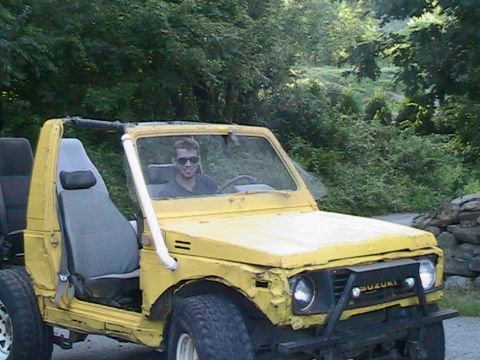 1987 Suzuki Samurai - A man smiles while driving a yellow Suzuki Samurai off-road.