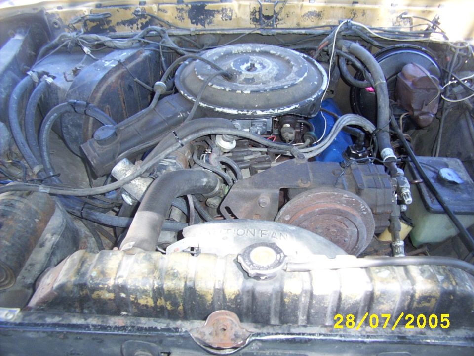 Carbureted engine with round air cleaner and fan in a rusty yellow engine compartment