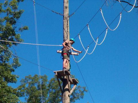 1995 Ford Bronco - A person is suspended on a wooden platform high up on a utility pole, preparing to zip line.