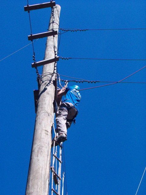 1995 Ford Bronco - A lineman ascends a utility pole using a rope ladder against a clear blue sky.