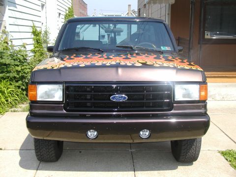 1991 Ford F-150 - A 1991 Ford F-150 truck is parked on a sidewalk, displaying flame decals on its hood.