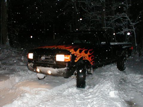 1991 Ford F-150 - A black pickup truck with flame decals is stuck in the snow at night.