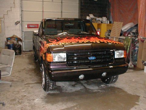 1991 Ford F-150 - This dark pickup truck features flame decals on the hood and a front-facing view, consistent with a 1991 Ford F-150.