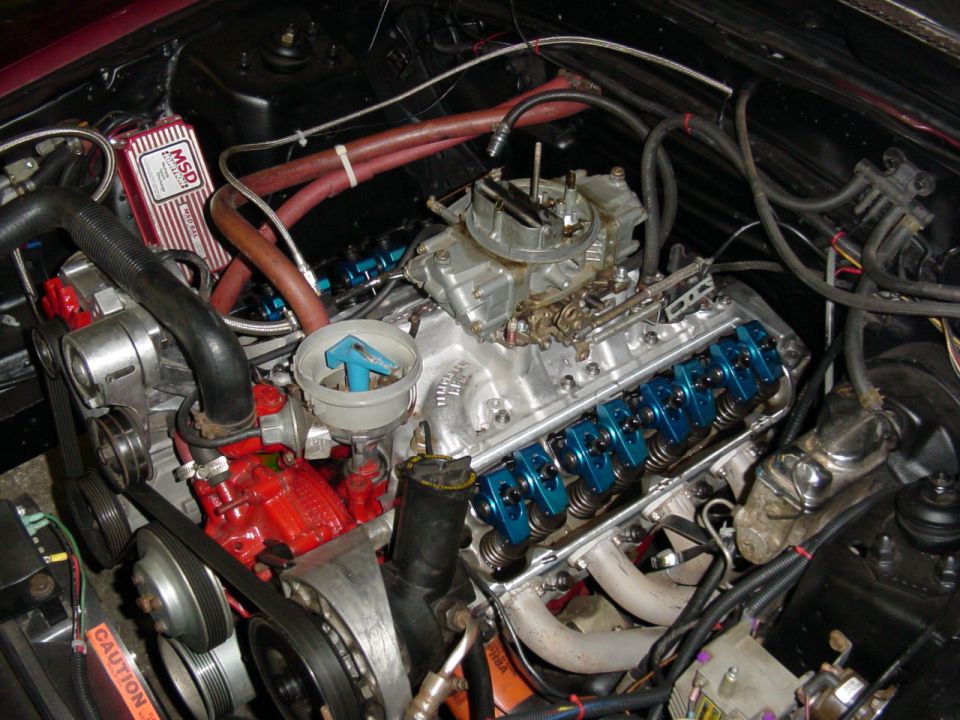 V8 engine with valve cover off showing blue rocker arms, carburetor, and red MSD ignition box