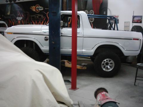 1978 Ford Bronco - White 1978 Ford Bronco with roll cage, lifted and on a shop lift, showing chrome trim and aftermarket wheels.